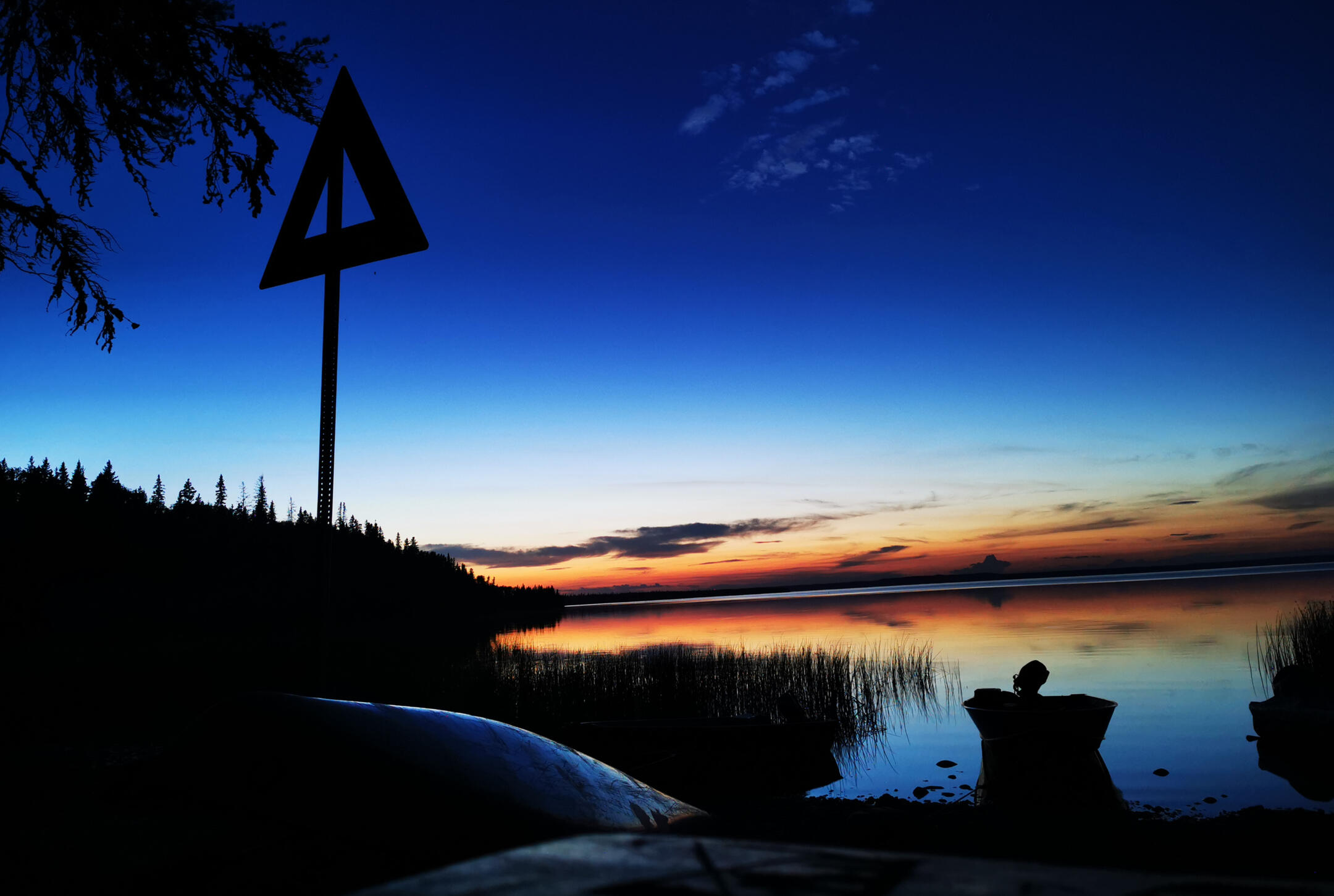 Sunset on a wilderness lakeshore with a boat and canoes in the foreground.